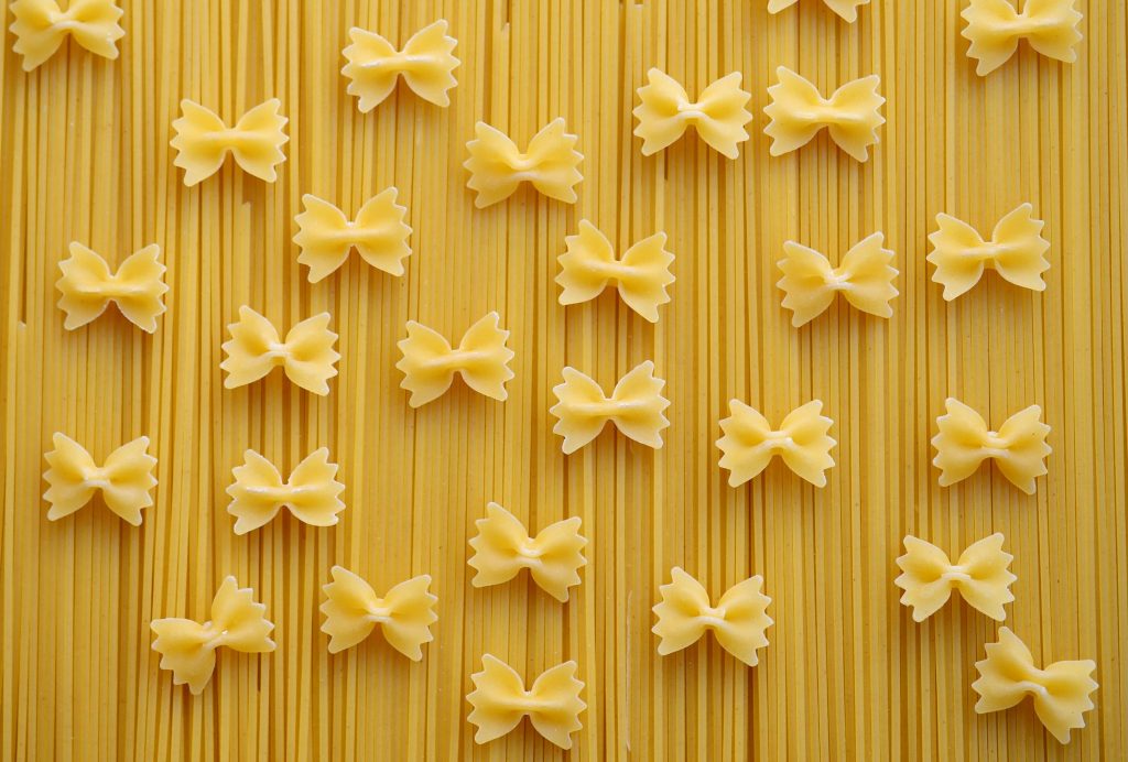 Flat lay of Italian pasta varieties, showcasing farfalle and spaghetti on a neutral background.