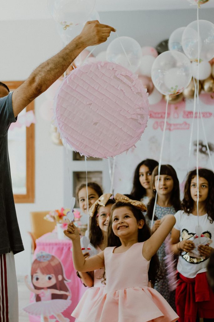 Smiling children having fun at a birthday party with a pink pinata indoors.